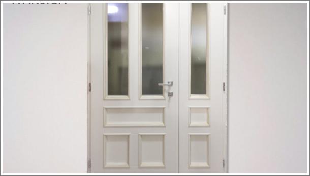 Dvokrilna bela ulazna drvena vrata, u gornjoj polovini peskareno staklo, u donjem delu drveni paneli, pogled sa unutrašnje strane